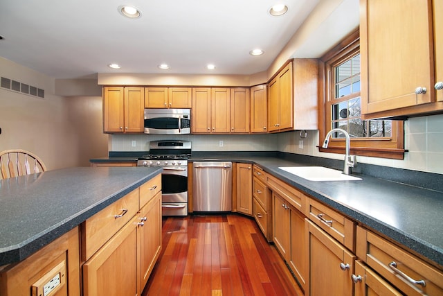 kitchen with dark countertops, visible vents, appliances with stainless steel finishes, and a sink