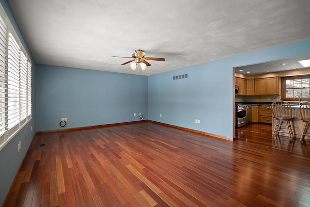 unfurnished living room featuring visible vents, dark wood-type flooring, ceiling fan, a sink, and baseboards