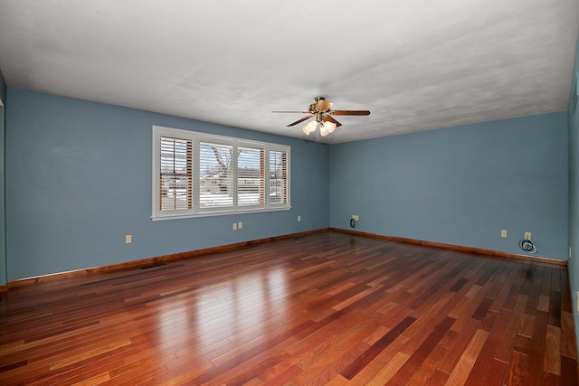 spare room with wood finished floors, a ceiling fan, and baseboards