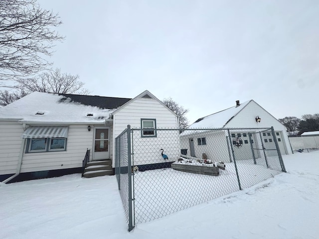 snow covered house featuring fence and an outbuilding