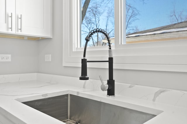 details featuring light stone counters, white cabinetry, and a sink