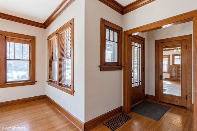 entryway featuring baseboards, light wood finished floors, ornamental molding, and visible vents