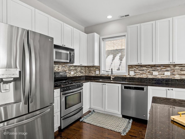 kitchen featuring stainless steel appliances, dark stone counters, backsplash, sink, and white cabinetry