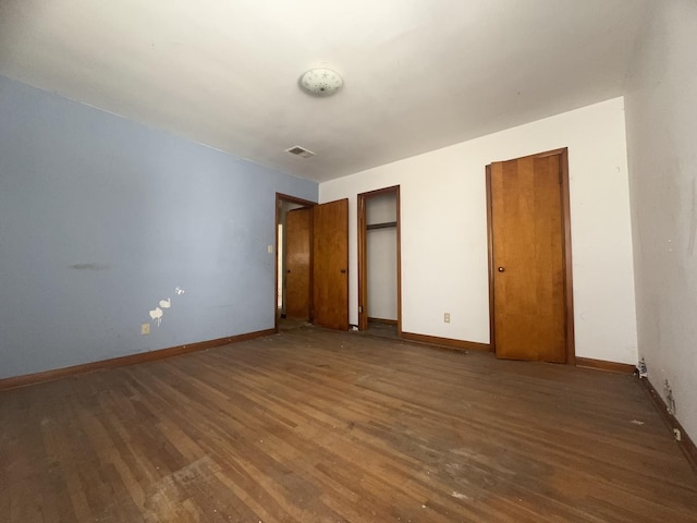 unfurnished bedroom featuring hardwood / wood-style floors and two closets