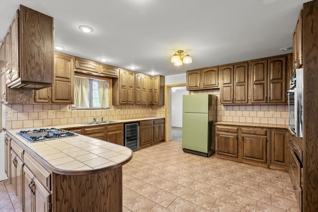 kitchen featuring wine cooler, a sink, appliances with stainless steel finishes, brown cabinets, and tasteful backsplash