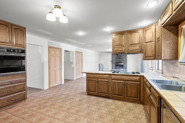 kitchen featuring tile counters, stainless steel gas stovetop, decorative backsplash, black oven, and a peninsula