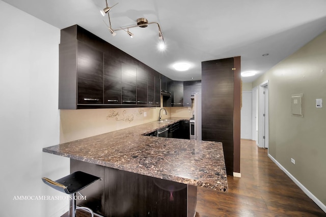 kitchen with a kitchen bar, dark wood-type flooring, a sink, a peninsula, and baseboards