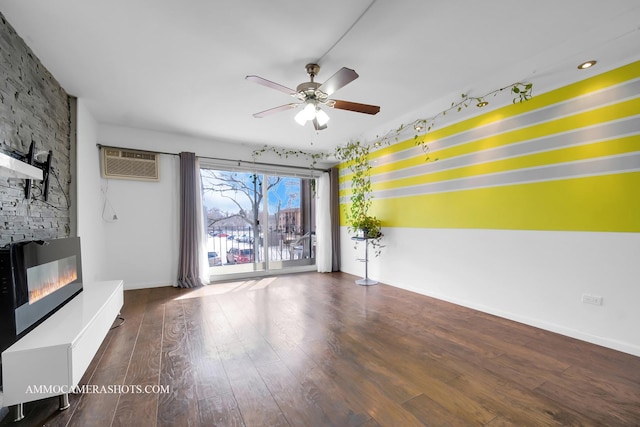 unfurnished living room with a large fireplace, wood finished floors, a ceiling fan, baseboards, and a wall mounted AC