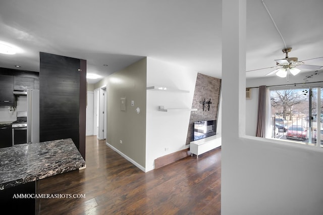 kitchen featuring a large fireplace, baseboards, dark stone countertops, dark wood-type flooring, and stainless steel range with gas cooktop