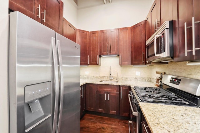 kitchen with sink, light stone counters, dark wood-type flooring, appliances with stainless steel finishes, and decorative backsplash