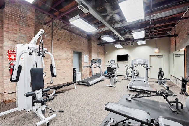 exercise room featuring brick wall and a towering ceiling