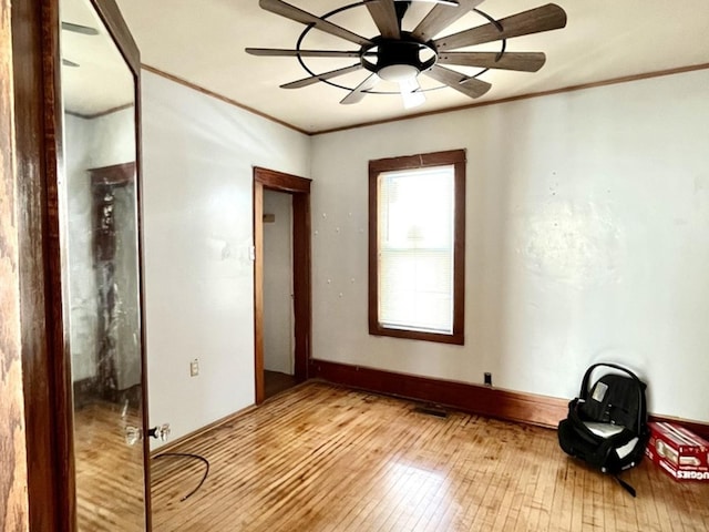 empty room featuring ornamental molding, light wood-type flooring, baseboards, and a ceiling fan