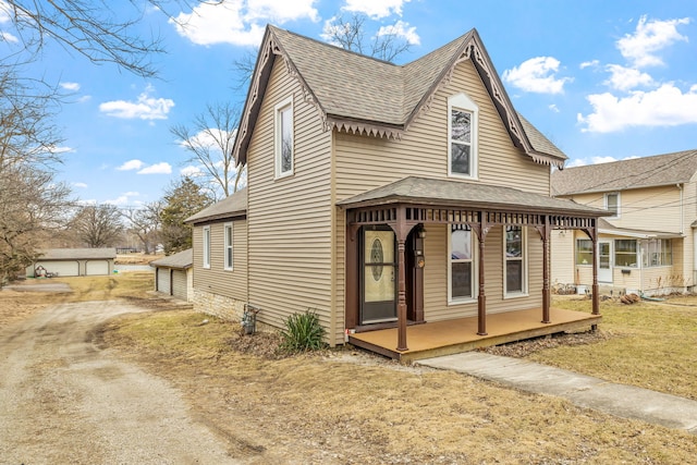 view of front of house with covered porch, roof with shingles, an outdoor structure, and a front yard