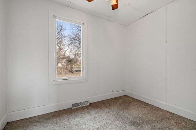 carpeted spare room with a drop ceiling, visible vents, and a ceiling fan