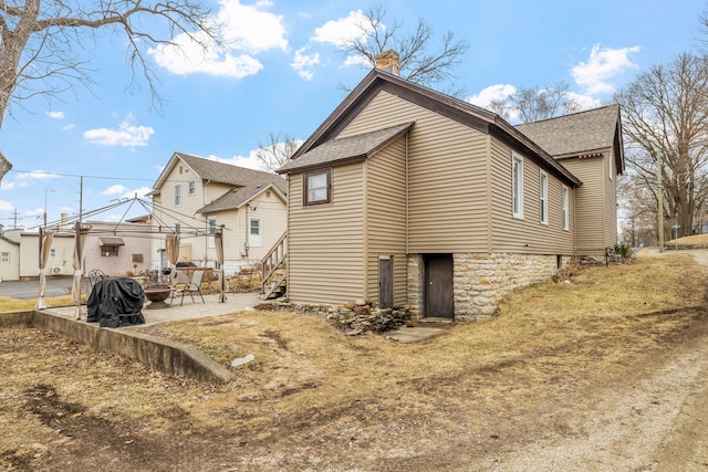 view of property exterior featuring a patio area, a shingled roof, a chimney, and a gazebo