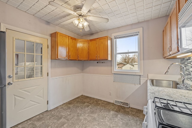 kitchen with range with gas stovetop, a wainscoted wall, light countertops, visible vents, and a sink