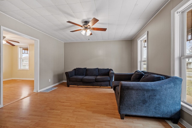 living room with light wood-style flooring, visible vents, ceiling fan, and baseboards