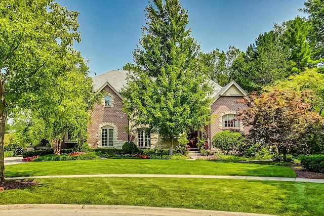 tudor-style house featuring brick siding and a front yard