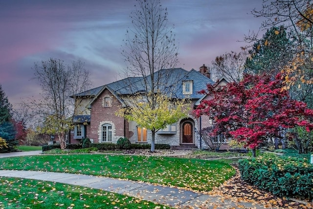 view of front of house with brick siding, a chimney, and a front yard