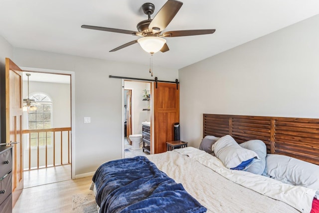 bedroom featuring a ceiling fan, baseboards, light wood-style floors, a barn door, and connected bathroom