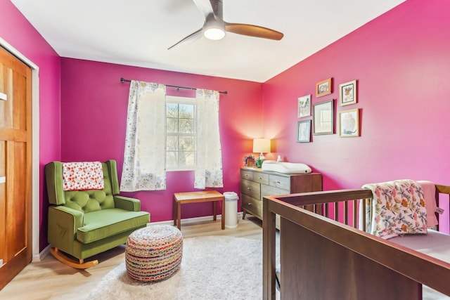 bedroom featuring baseboards, a ceiling fan, a nursery area, and wood finished floors