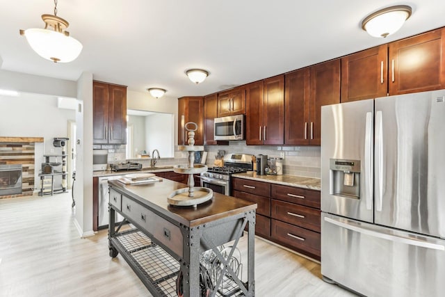 kitchen featuring light wood-style flooring, a sink, decorative light fixtures, backsplash, and appliances with stainless steel finishes