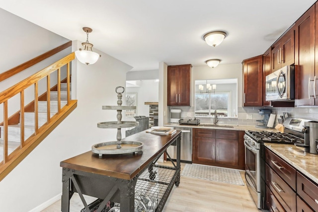 kitchen with a sink, light stone counters, tasteful backsplash, stainless steel appliances, and hanging light fixtures