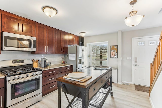 kitchen with decorative light fixtures, decorative backsplash, light wood-style flooring, and stainless steel appliances