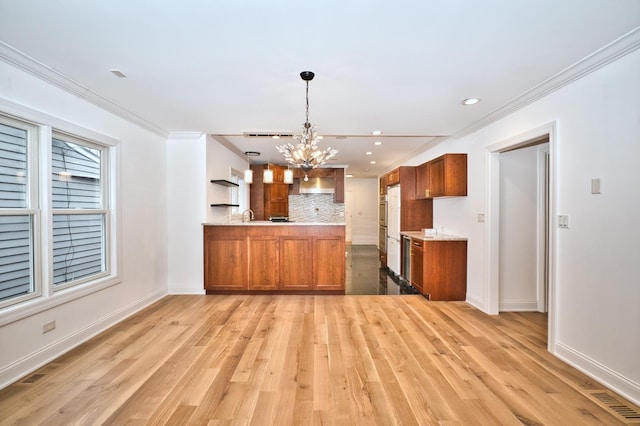 kitchen with backsplash, light countertops, brown cabinets, a peninsula, and an inviting chandelier