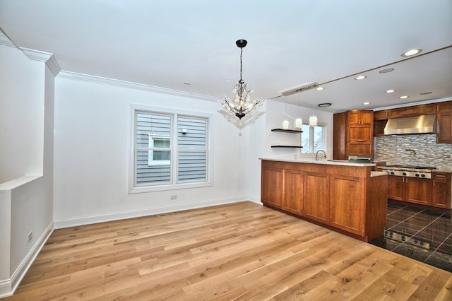 kitchen with tasteful backsplash, ventilation hood, stainless steel gas stovetop, a peninsula, and a chandelier