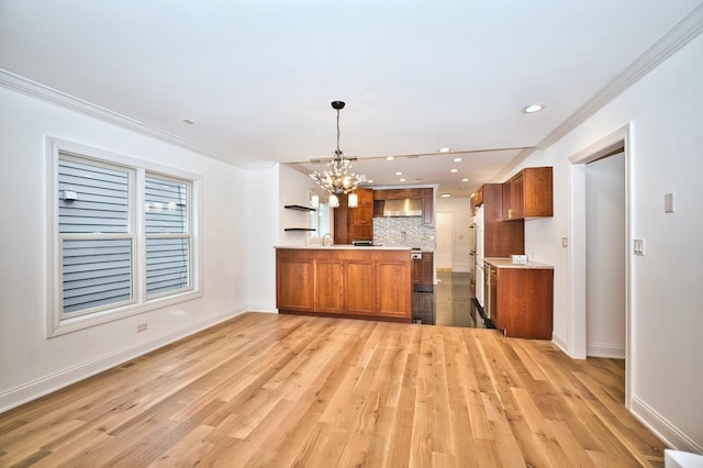 kitchen with a peninsula, a notable chandelier, wall chimney exhaust hood, and brown cabinets