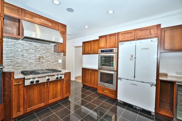 kitchen featuring brown cabinetry, ornamental molding, decorative backsplash, appliances with stainless steel finishes, and wall chimney exhaust hood