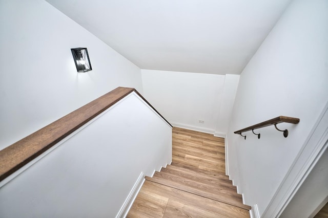 stairway featuring lofted ceiling, wood finished floors, and baseboards