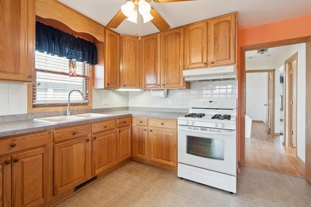 kitchen with visible vents, brown cabinetry, white range with gas cooktop, a sink, and under cabinet range hood