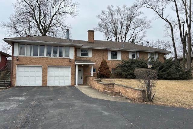 view of front of house featuring a garage, brick siding, driveway, and a chimney