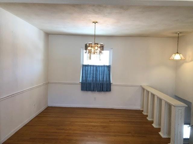 empty room with a chandelier, dark wood-style flooring, and baseboards