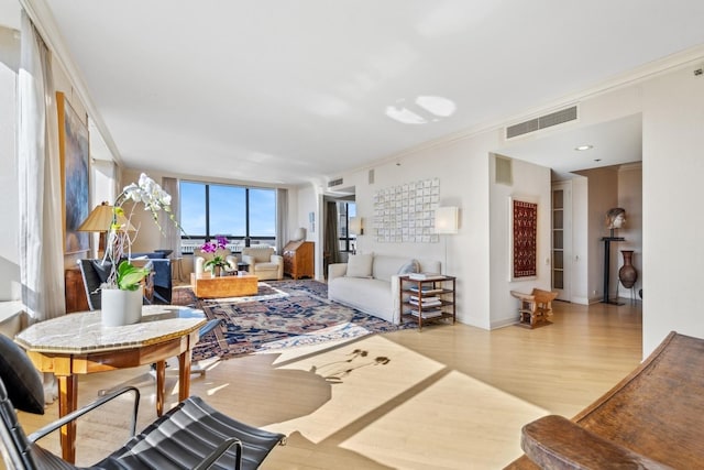 living room featuring ornamental molding, light wood finished floors, visible vents, and baseboards