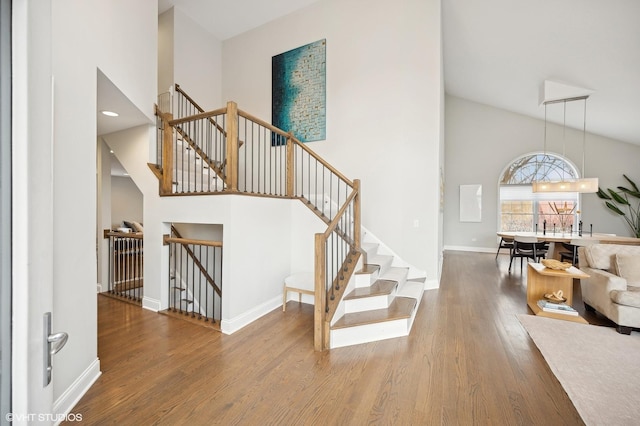 stairs featuring high vaulted ceiling, wood finished floors, and baseboards