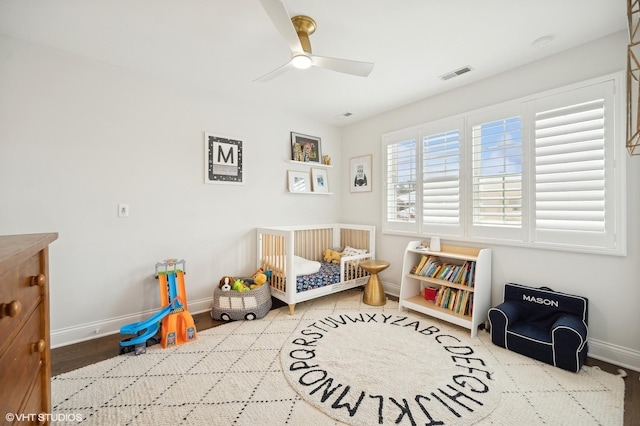 bedroom featuring a crib, baseboards, visible vents, and a ceiling fan