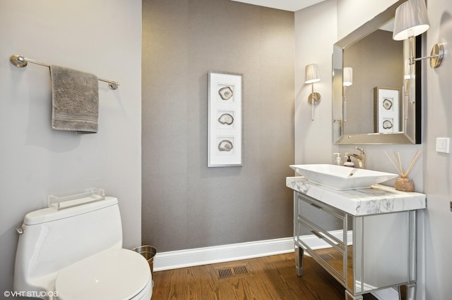 half bathroom with baseboards, visible vents, toilet, wood finished floors, and vanity