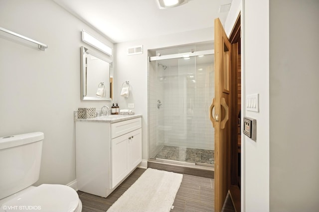 bathroom with visible vents, toilet, a stall shower, vanity, and wood finished floors