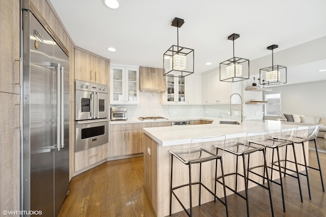 kitchen featuring modern cabinets, appliances with stainless steel finishes, dark wood-type flooring, light brown cabinets, and a sink