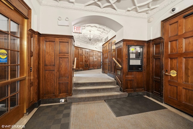 hall with carpet flooring, crown molding, wood walls, and coffered ceiling