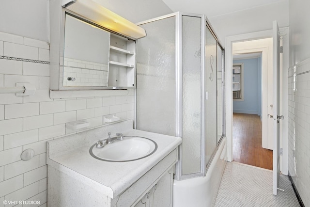 bathroom with tile walls, combined bath / shower with glass door, and vanity