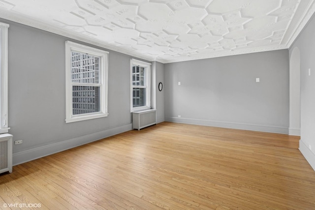 spare room with radiator, ornamental molding, and light wood-type flooring