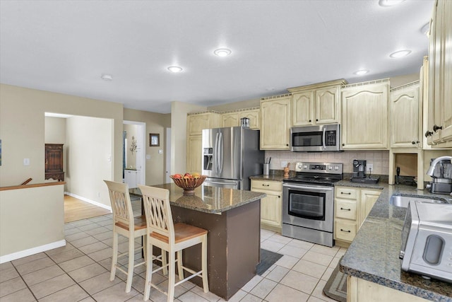 kitchen featuring light tile patterned flooring, a sink, appliances with stainless steel finishes, backsplash, and a kitchen bar