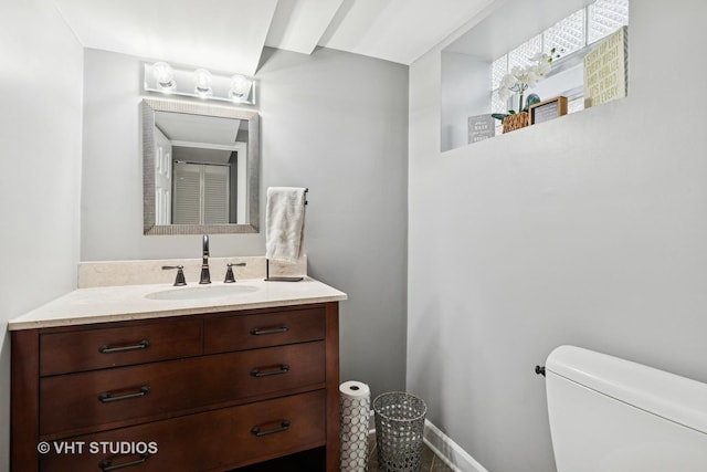 half bathroom featuring toilet, baseboards, and vanity