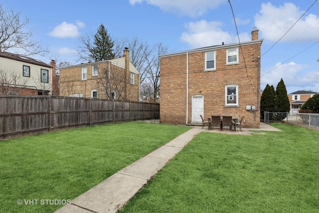 rear view of house featuring a lawn, a fenced backyard, a chimney, a patio area, and brick siding