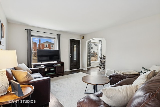 living room with arched walkways, dark wood-style flooring, visible vents, and baseboards