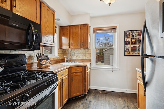 kitchen featuring black microwave, a sink, range with gas stovetop, freestanding refrigerator, and decorative backsplash